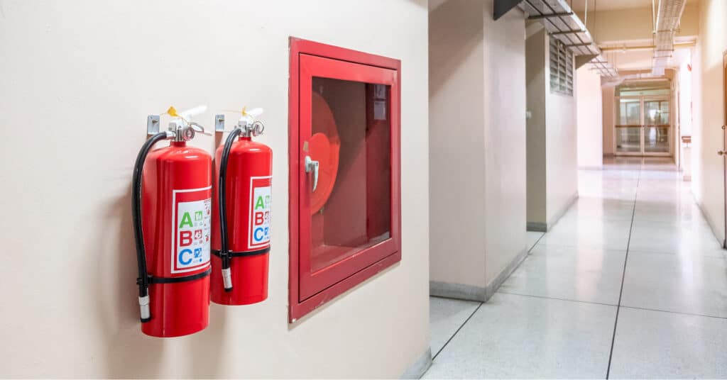 A picture of a corridor inside a building, with two fire extinguishers hung on the wall.