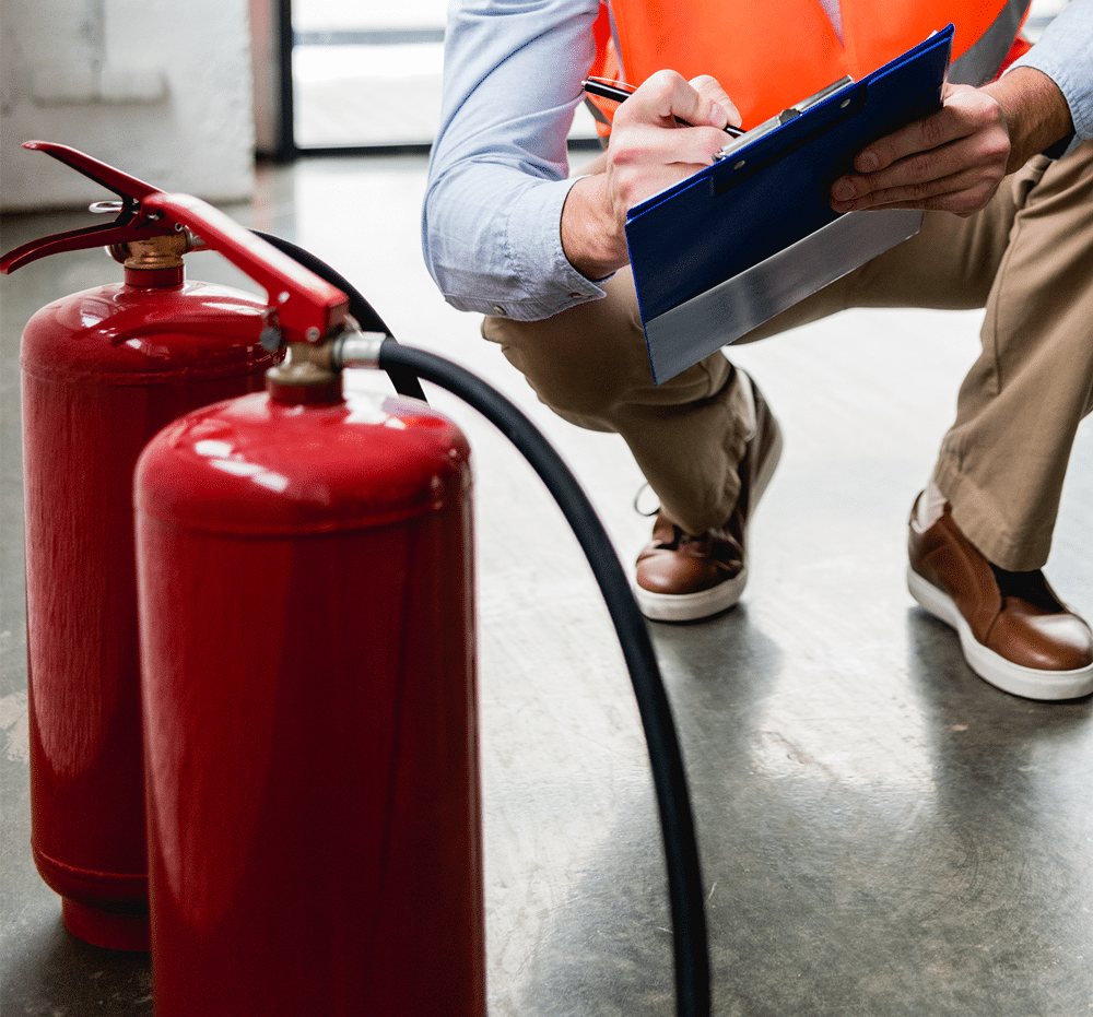 Fire extinguishers on the floor and man with clipboard doing a fire safety inspection