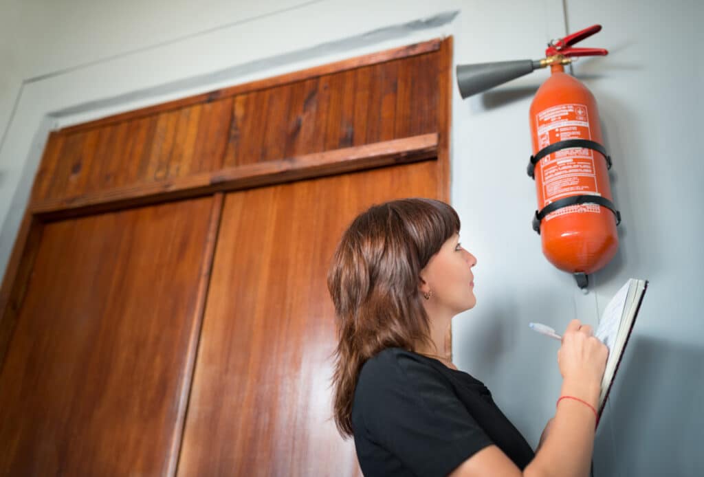 A woman inspects a fire extinguisher and writes notes.