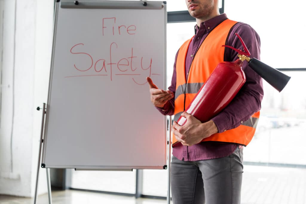 A fire safety instructor holding a fire extinguisher and standing by a flipchart that reads “Fire Safety”.