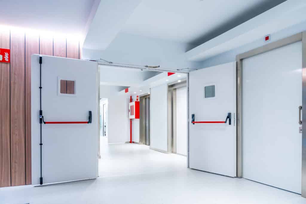 A set of double fire doors held open in a white hospital corridor.