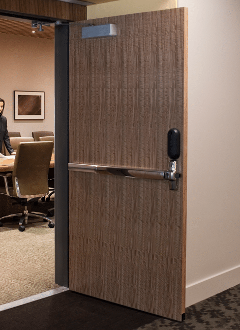 A large wooden internal fire door, open to show a conference room. The firs door has a long handle and a door closer