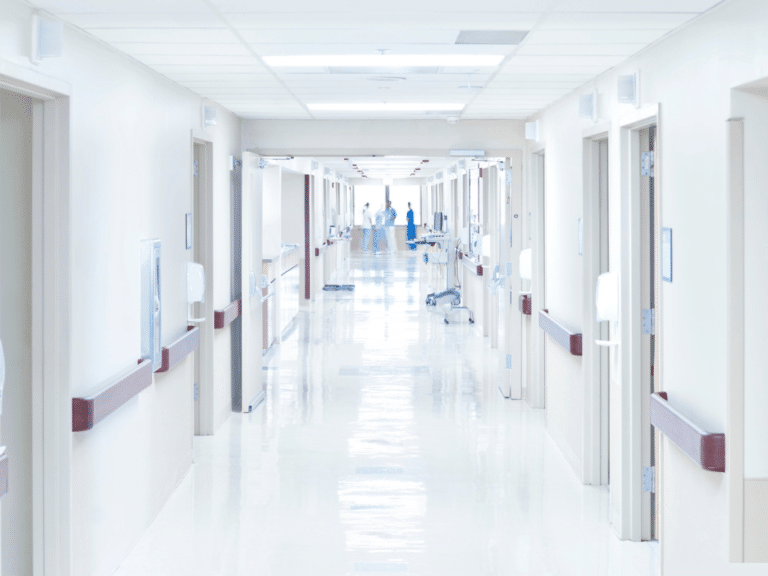 A long white corridor in a hospital showing numerous fire doors at either side of the corridor.